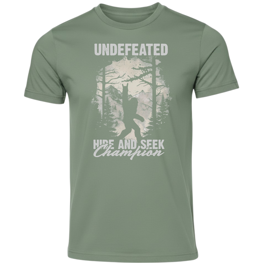 An olive green short-sleeve t-shirt with a distressed white graphic on the front featuring a Bigfoot silhouette in a forest and the text 'UNDEFEATED' and 'HIDE AND SEEK Champion'.