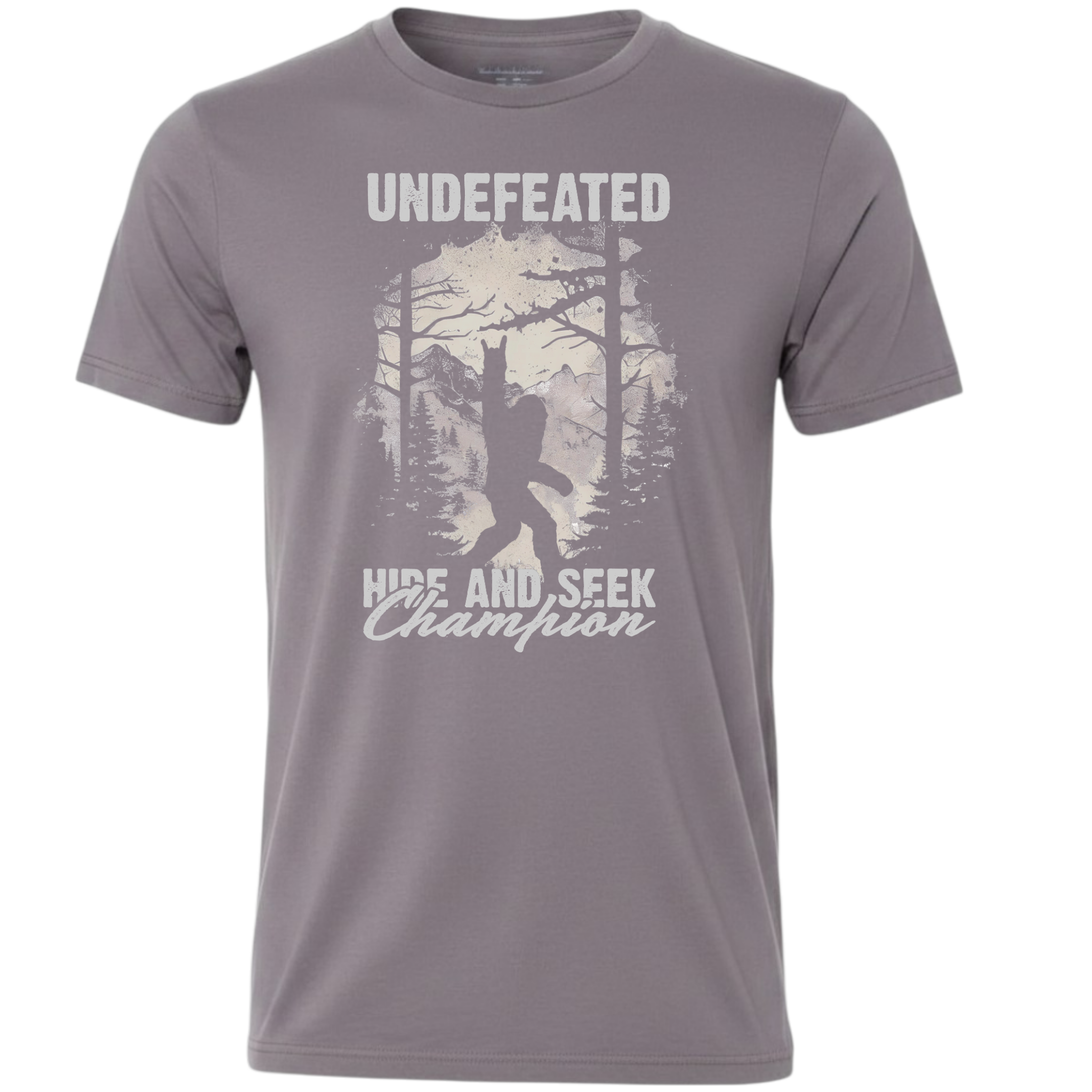 A gray short-sleeve crewneck t-shirt featuring a white graphic print of a Bigfoot silhouette in a forest, with the text 'UNDEFEATED' above and 'HIDE AND SEEK Champion' below.