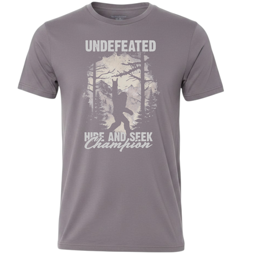 A gray short-sleeve crewneck t-shirt featuring a white graphic print of a Bigfoot silhouette in a forest, with the text 'UNDEFEATED' above and 'HIDE AND SEEK Champion' below.