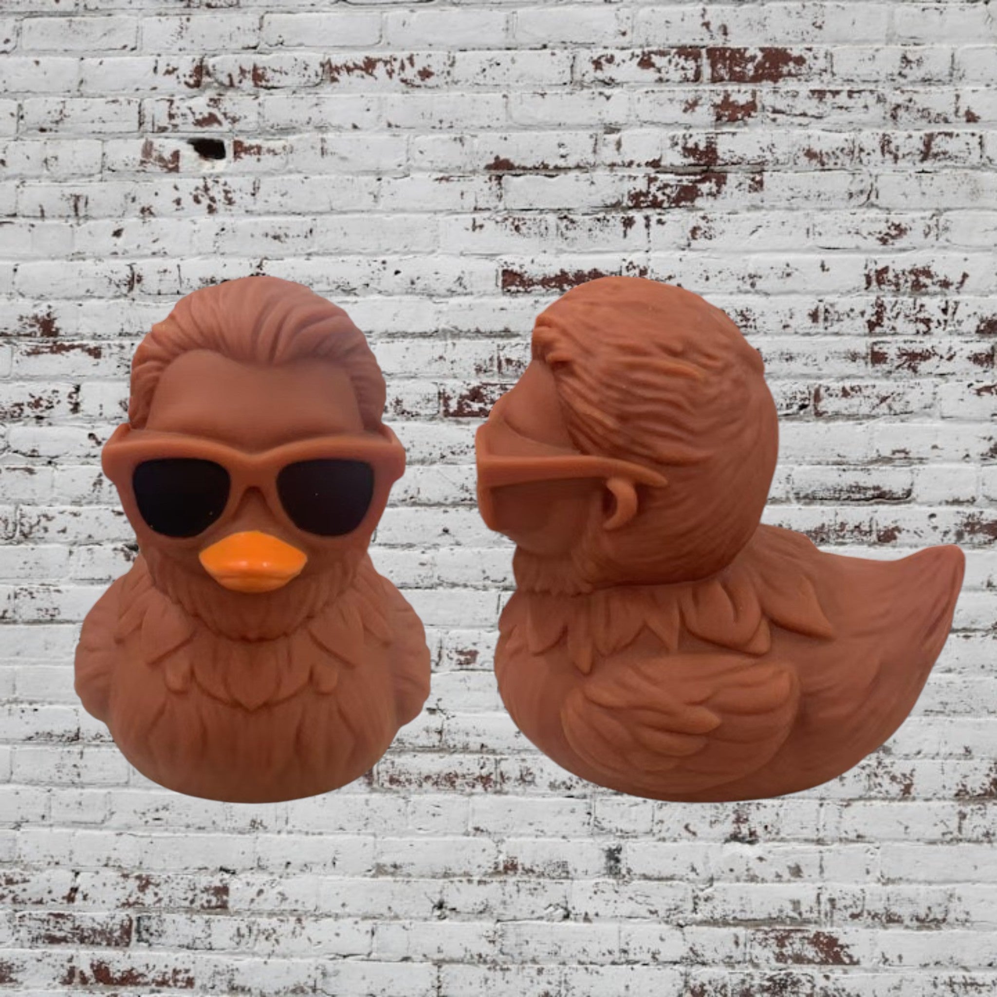 Two terracotta-colored rubber ducks against a white brick wall background. One duck is facing forward and wearing black sunglasses with an orange beak.